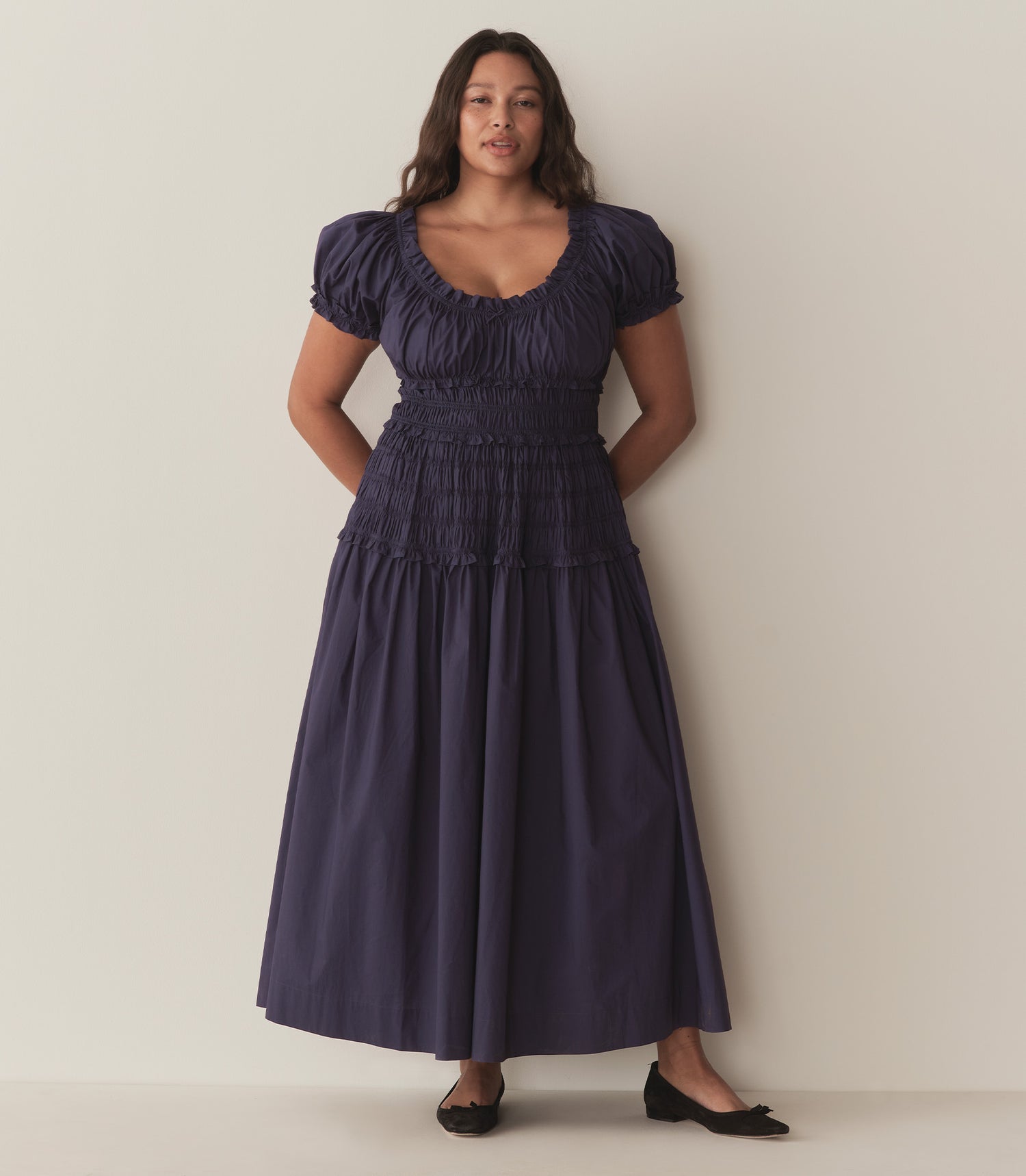 Alana wears a dark blue dress with puffed sleeve and ruching along the bodice.