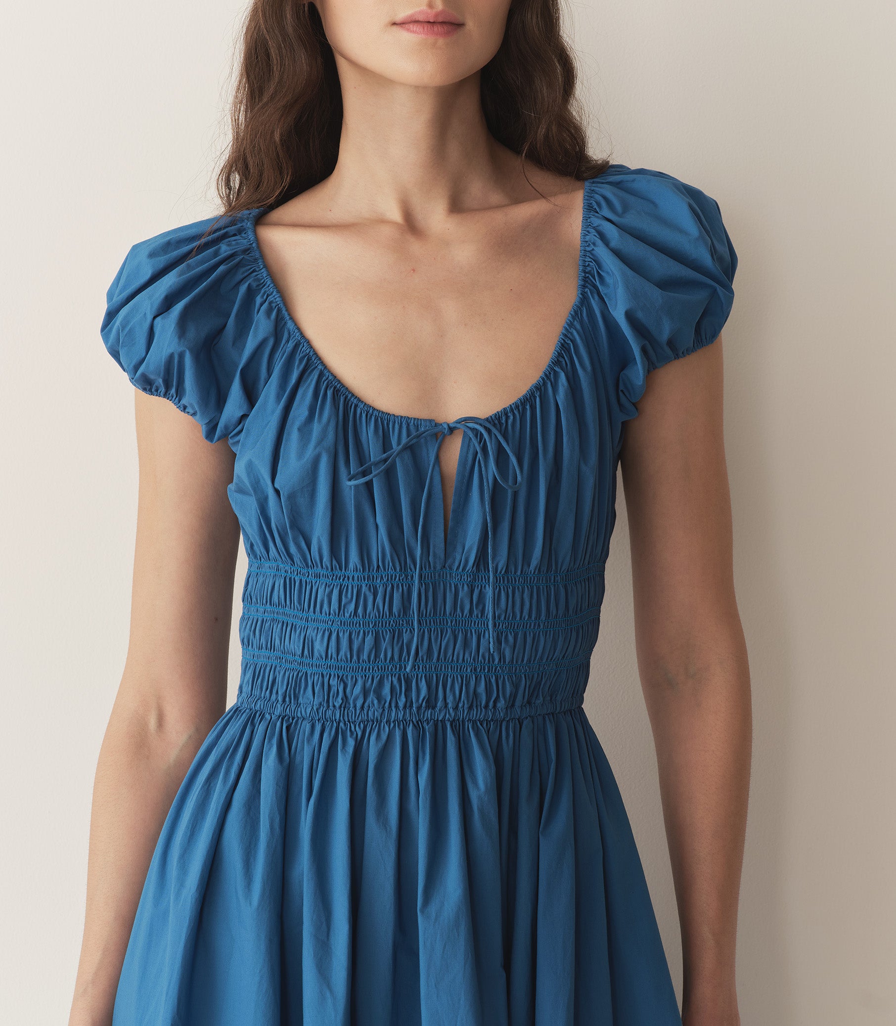 Bruna is wearing a long blue cotton dress with short puff sleeves and sandals. 2